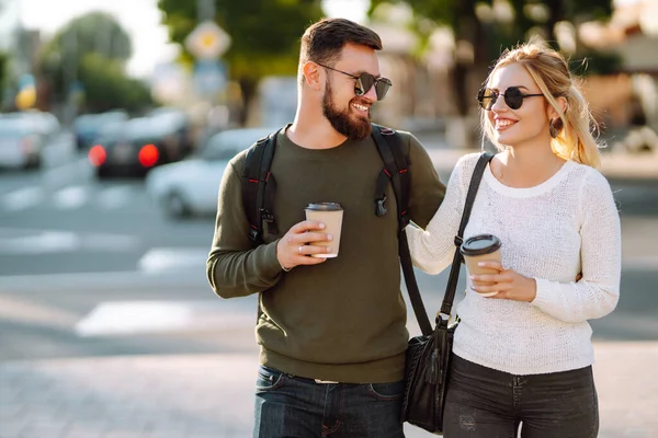 スタイリッシュな男女が街の通りを歩き 一緒にコーヒーを飲む 恋するカップルは朝の街を歩きながらコミュニケーションをとります 人間関係 リラクゼーションの概念 — ストック写真