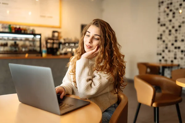 Genç serbest çalışan bir kadın, bir kafede oturup internette çalışıyor. Eğitim kavramı, serbest çalışma..