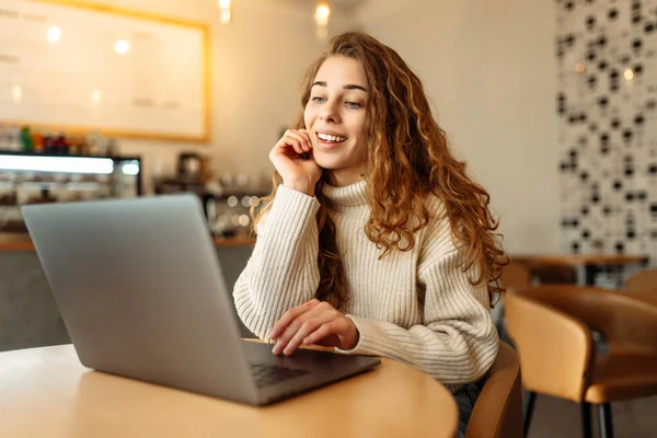 Genç serbest çalışan bir kadın, bir kafede oturup internette çalışıyor. Eğitim kavramı, serbest çalışma..