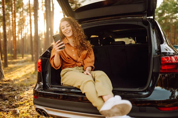 Young Curly Woman Stylish Clothes Trunk Car Forest Uses Phone — Stock Photo, Image