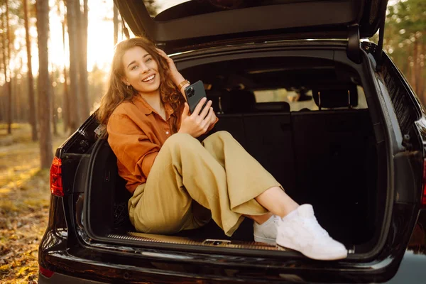 Young Curly Woman Stylish Clothes Trunk Car Forest Uses Phone — Stock Photo, Image