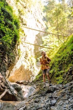 Yürüyüş yapan sarı sırt çantalı bir gezgin yeni yerleri keşfeder, dereden su toplar, dağlara tırmanır ve orman boyunca yürüyüş yapar..