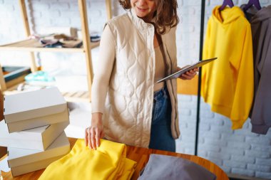 İşyerindeki dijital tabletli mutlu küçük işletme sahibi. Genç bir iş kadını giyim mağazasından siparişleri kontrol ediyor. Alışveriş konsepti, moda.