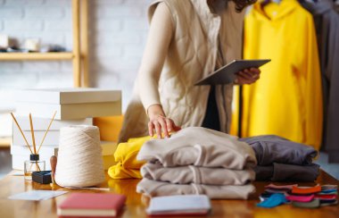 İşyerindeki dijital tabletli mutlu küçük işletme sahibi. Genç bir iş kadını giyim mağazasından siparişleri kontrol ediyor. Alışveriş konsepti, moda.