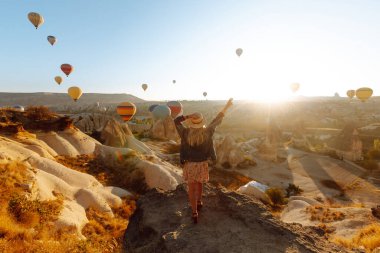 Şapkalı kadın turist sırtı dağda duruyor, Türkiye 'nin başkenti Kapadokya' daki balonlara bakıyor. Dağın tepesinde güzel bir kadın güzel bir manzaranın tadını çıkarıyor.. 