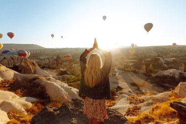 Şapkalı kadın turist sırtı dağda duruyor, Türkiye 'nin başkenti Kapadokya' daki balonlara bakıyor. Dağın tepesinde güzel bir kadın güzel bir manzaranın tadını çıkarıyor.. 