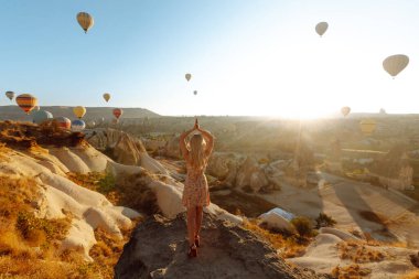 Şapkalı kadın turist sırtı dağda duruyor, Türkiye 'nin başkenti Kapadokya' daki balonlara bakıyor. Dağın tepesinde güzel bir kadın güzel bir manzaranın tadını çıkarıyor.. 
