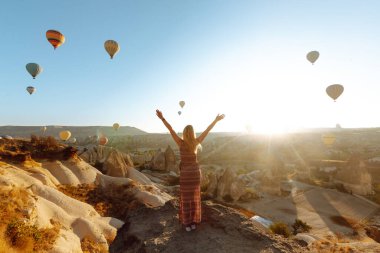 Şapkalı kadın turist sırtı dağda duruyor, Türkiye 'nin başkenti Kapadokya' daki balonlara bakıyor. Dağın tepesinde güzel bir kadın güzel bir manzaranın tadını çıkarıyor.. 