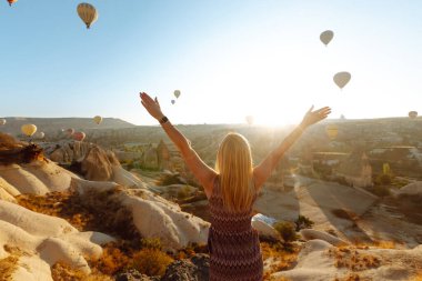 Şapkalı kadın turist sırtı dağda duruyor, Türkiye 'nin başkenti Kapadokya' daki balonlara bakıyor. Dağın tepesinde güzel bir kadın güzel bir manzaranın tadını çıkarıyor.. 