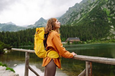 Slovakya 'yı, Avrupa' yı dolaş. Sarı sırt çantalı bir turist bir dağ gölünün arka planında duruyor. Özgürlük konsepti, turizm, yürüyüş, doğa