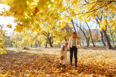 Mutlu genç anne ve kız birlikte sonbahar parkında yürürken vakit geçiriyorlar. Anne ve çocuk sonbaharda dışarıda eğleniyorlar. Rahatlama, çocukluk, eğlence kavramı..