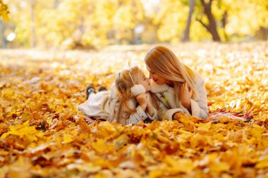 Mutlu genç anne ve kız birlikte sonbahar parkında yürürken vakit geçiriyorlar. Anne ve çocuk sonbaharda dışarıda eğleniyorlar. Rahatlama, çocukluk, eğlence kavramı..