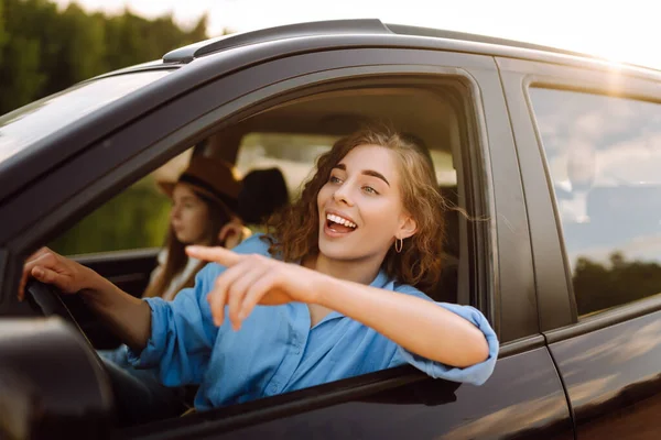 Two women travelers travel by car, have fun. Beautiful female friends in the car enjoy a car trip together. Travel, tourism.