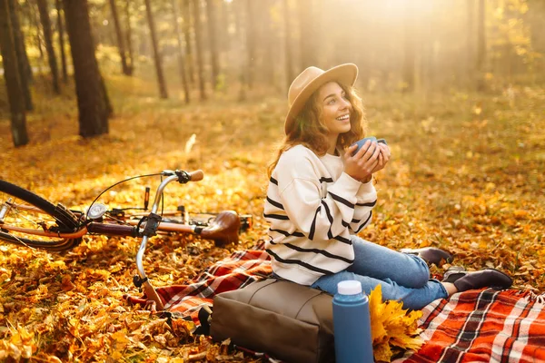 帽子の中の美しいカーリーな女性は 秋の森で魔法使いと赤いマットの上に座っています 女性はミニピクニックで自然を楽しんでいます リラクゼーション 自然の概念 — ストック写真