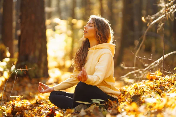 Beautiful woman practices yoga in the autumn forest. Lifestyle and meditation concept.