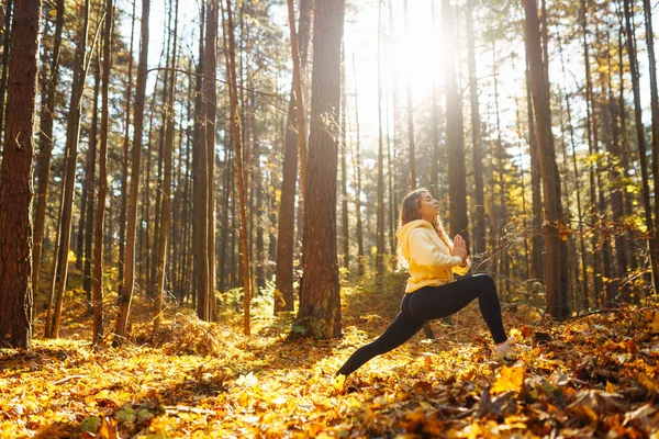 Beautiful woman practices yoga in the autumn forest. Lifestyle and meditation concept.