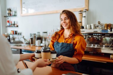 Paket yemek konsepti. Güzel bir bayan barista müşterisine paket kahve verir. Küçük bir işletme sahibi, barın arkasında bir kahve dükkanı var. İş konsepti.