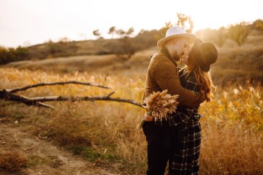 Stylish woman and a man are relaxing in nature. Couple in love enjoying time together while walking at sunset in autumn. Concept of people, style, love, relaxation. clipart