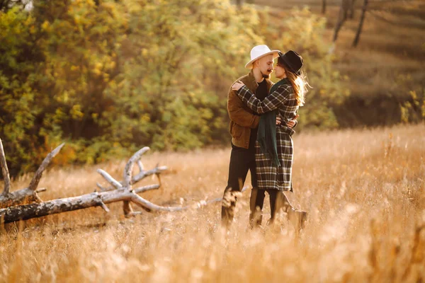 Stylish woman and a man are relaxing in nature. Couple in love enjoying time together while walking at sunset in autumn. Concept of people, style, love, relaxation.