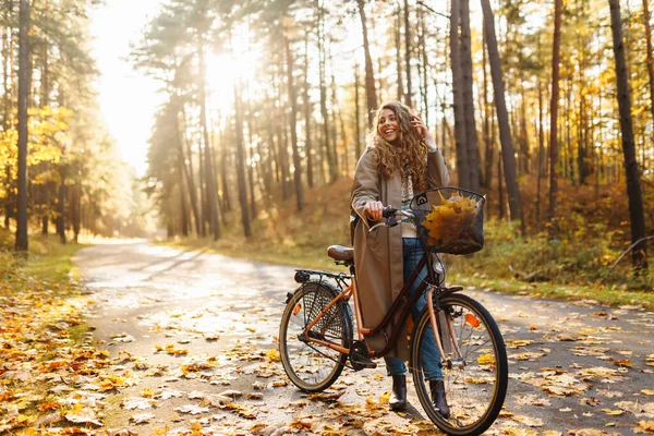Happy active woman in stylish clothes rides a bicycle in an autumn park at sunset. Outdoor portrait. Beautiful woman enjoying nature. Active lifestyle.