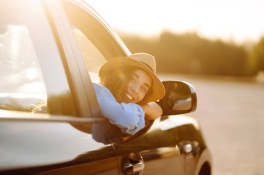 Araba camından sarkan gülümseyen turist maceranın tadını çıkarıyor, özgürlüğü hissediyor, arabayla seyahat ediyor. Macera, tatil, rahatlama kavramı..