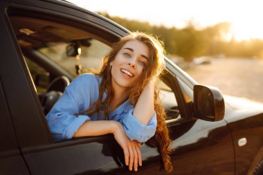 Araba camından sarkan gülümseyen turist maceranın tadını çıkarıyor, özgürlüğü hissediyor, arabayla seyahat ediyor. Macera, tatil, rahatlama kavramı..