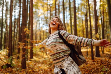 Sırt çantalı bir turist, sonbahar ormanında bir patika boyunca yürüyor. Güzel bir kadın doğada güneşli bir günün tadını çıkarır, özgürlüğü hisseder ve temiz havayı soluyarak doğayı keşfeder..