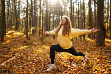 Genç bir kadın sonbahar ormanında, düşmüş yapraklar üzerinde yoga egzersizleri yapıyor. Yaşam tarzı, meditasyon konsepti. Eğleniyorum..