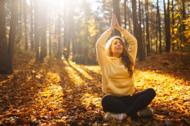 Genç bir kadın sonbahar ormanında, düşmüş yapraklar üzerinde yoga egzersizleri yapıyor. Yaşam tarzı, meditasyon konsepti. Eğleniyorum..