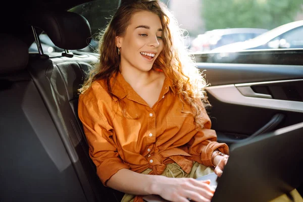 車の後部座席に座っている現代的なラップトップを持つ若いビジネス女性 成功したスタートアップ リモートワーク テクノロジーの概念 フリーランス — ストック写真
