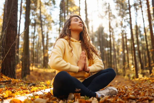 Genç bir kadın sonbahar ormanında, düşmüş yapraklar üzerinde yoga egzersizleri yapıyor. Yaşam tarzı, meditasyon konsepti. Eğleniyorum..