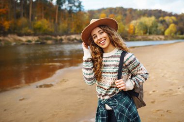 Sırt çantası ve şapkası olan yürüyüş botları giyen kadın gezgin doğayı keşfediyor. Nehrin kıyısındaki kumsalda duran bir kadın manzaranın ve güneşli havanın tadını çıkarıyor, özgürlüğü hissediyor..