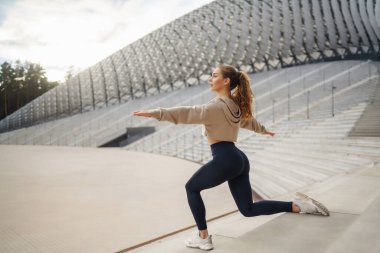 Sokakta egzersiz yapan sporcu bir kadın. Spor giyimli bir kadın spor için içeri girer, güneşli bir günde dışarıda egzersiz yapar. Spor anlayışı, aktivite.
