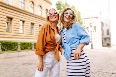 Mutlu iki arkadaş şehirde gülümseyerek poz veriyor. Güzel kadınların hafta sonu eğlenirken, seyahat ederken çekilmiş sokak fotoğrafı. Seyahat, macera konsepti.
