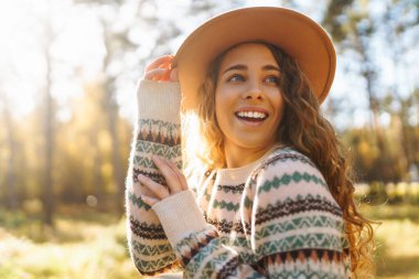 Şık bir süveter ve şapka giyen güzel bir kadın sonbahar ormanında yürüyor, doğanın tadını çıkarıyor, özgürlüğü hissediyor. Doğa kavramı, rahatlama..