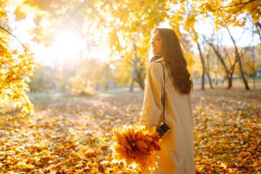 Retro kameralı, açık renk ceketli gülümseyen kadın sonbahar ormanlarında eğleniyor. Mutlu ruh hali, boş zaman. Yaşam tarzı kavramı.
