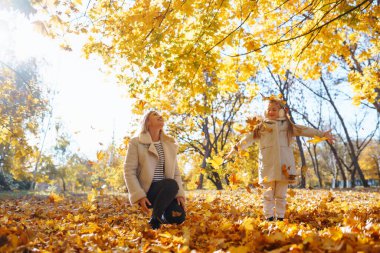 Sonbahar sarı yapraklı küçük kızı ve annesi sonbaharda bir şehir parkında birlikte eğleniyorlar. Çocukluk konsepti, yürüyüşler, hafta sonları.