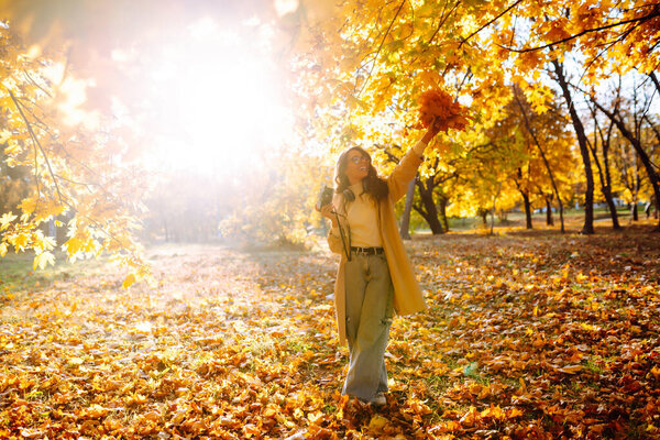 Smiling woman in a light coat with a retro camera spends time having fun in the autumn forest. Happy mood, leisure time. Lifestyle concept.