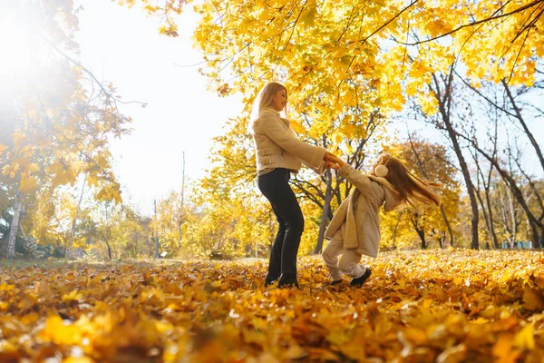Little daughter and her mother with autumn yellow leaves have fun together in a city park in autumn. Childhood concept, walks, weekends.