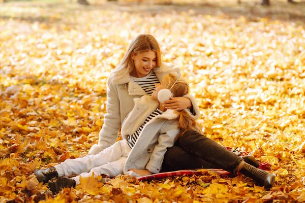 Little daughter and her mother with autumn yellow leaves have fun together in a city park in autumn. Childhood concept, walks, weekends.