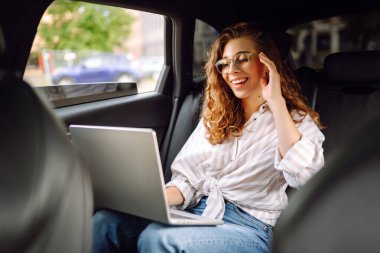 Dizüstü bilgisayarı olan şık bir kadın arabanın arka koltuğunda çalışıyor. İnternette çalışıyorum. İş seyahati. Teknoloji konsepti.