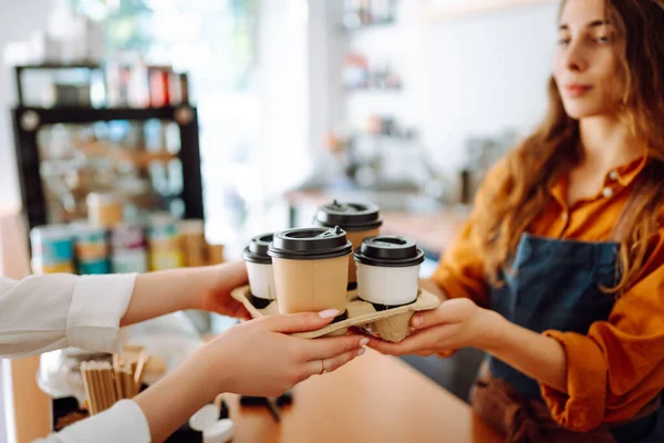 Close-up of a female barista\'s hands giving out a to-go drink order. The coffee shop owner gives orders to go. Takeaway drinks concept, small business.