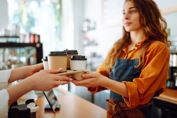 Close-up of a female barista\'s hands giving out a to-go drink order. The coffee shop owner gives orders to go. Takeaway drinks concept, small business.