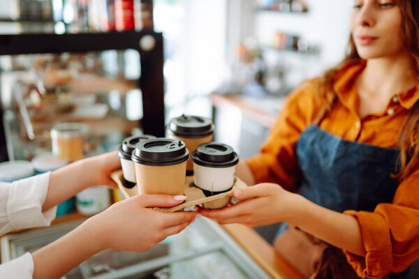 Close-up of a female barista's hands giving out a to-go drink order. The coffee shop owner gives orders to go. Takeaway drinks concept, small business.