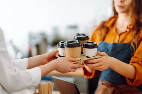 Close-up of a female barista's hands giving out a to-go drink order. The coffee shop owner gives orders to go. Takeaway drinks concept, small business.