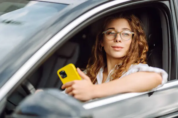 Güzel bayan sürücü arabada akıllı telefon kullanır. Araba kullanan bir kadın park ücretini ödemek ve şehirde dolaşmak için cep telefonu kullanıyor..