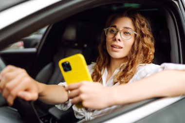 Güzel bayan sürücü arabada akıllı telefon kullanır. Araba kullanan bir kadın park ücretini ödemek ve şehirde dolaşmak için cep telefonu kullanıyor..