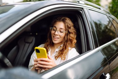 Güzel bayan sürücü arabada akıllı telefon kullanır. Araba kullanan bir kadın park ücretini ödemek ve şehirde dolaşmak için cep telefonu kullanıyor..