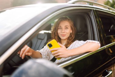 Güzel bayan sürücü arabada akıllı telefon kullanır. Araba kullanan bir kadın park ücretini ödemek ve şehirde dolaşmak için cep telefonu kullanıyor..