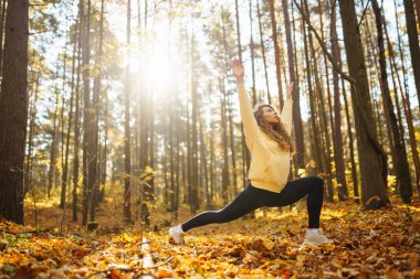 Spor giyim sektöründe aktif bir kadın sonbahar ormanında düşen yapraklar üzerinde yoga egzersizleri yapıyor, zen, meditasyon, rahatlama yapıyor. Rahatlama, özgürlük kavramı..